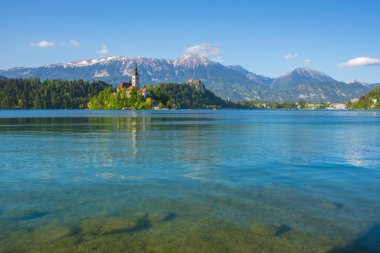 Bled Gölü 'nde güneşli bir sabah ve arka planda Julian Alps. Göl adası ve Mary 'nin Varsayımına adanmış küçük sevimli kilise Slovenya' daki ünlü turistik merkezlerdir.