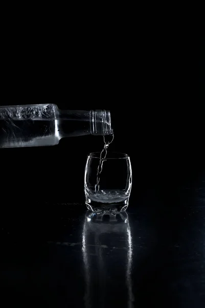 Vodka garrafa derramado em um copo no fundo preto — Fotografia de Stock