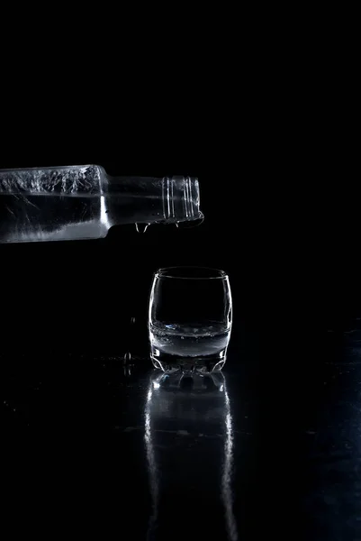 Vodka garrafa derramado em um copo no fundo preto — Fotografia de Stock