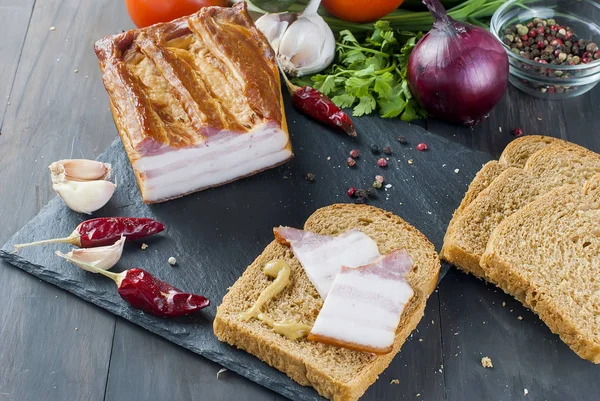 Bacon defumado com baguete e legumes em placa preta de pedra — Fotografia de Stock