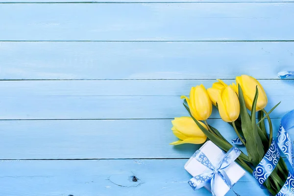 Bouquet of yellow tulips and a gift with a blue ribbon on a blue — Stock Photo, Image