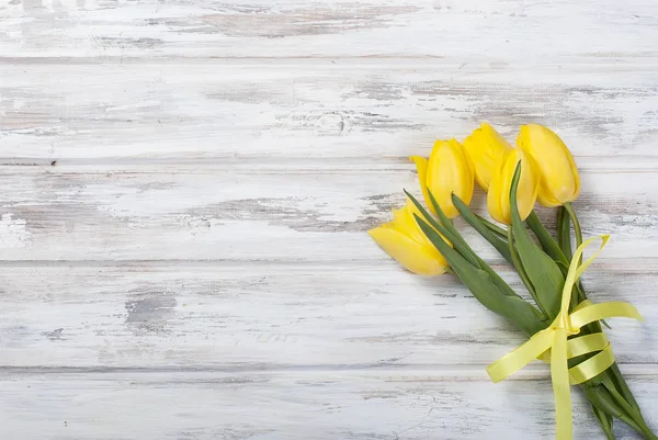 bouquet of yellow tulips and a gift with a yellow ribbon on a wo