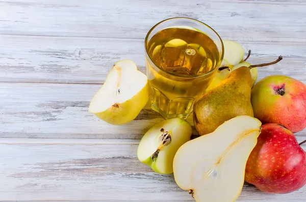 Juice i ett glas och en mogna äpplen och päron på ett träbord — Stockfoto