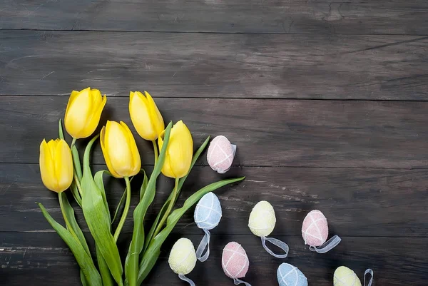 Buquê de tulipas amarelas e ovos de páscoa coloridos em um bac de madeira — Fotografia de Stock