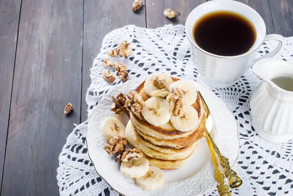 Pancakes with banana, nuts ,honey and cup coffee on dark backgro