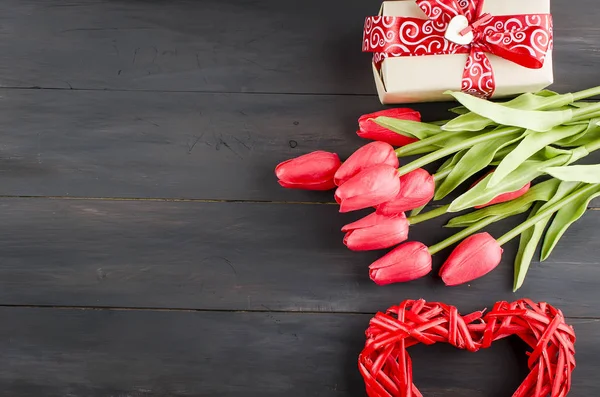 Сердце из плетеного мешка, подарочная коробка и тюльпаны на деревянной доске — стоковое фото