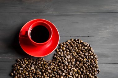 Siyah kırmızı Kupası kahve ve koyu ahşap zemin üzerine kahve tanelerinin bir kalp şeklinde dağılmış. Uzay kopyalayın. Üstten Görünüm