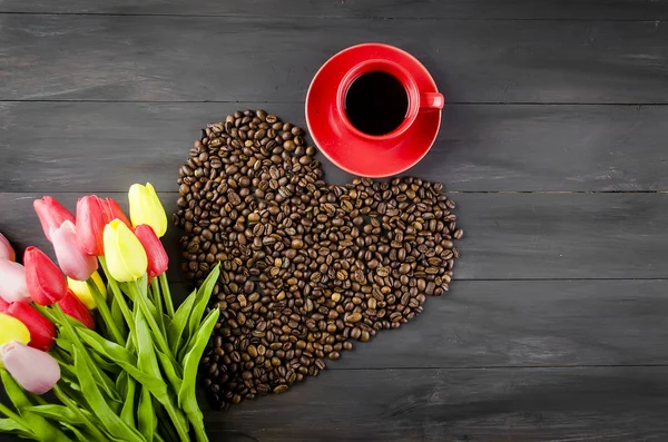 Coffee cup and scattered in the form of a heart of coffee grains on dark wooden background. bouquet of tulips and coffee declaration of love. Copy space. valentines day concept