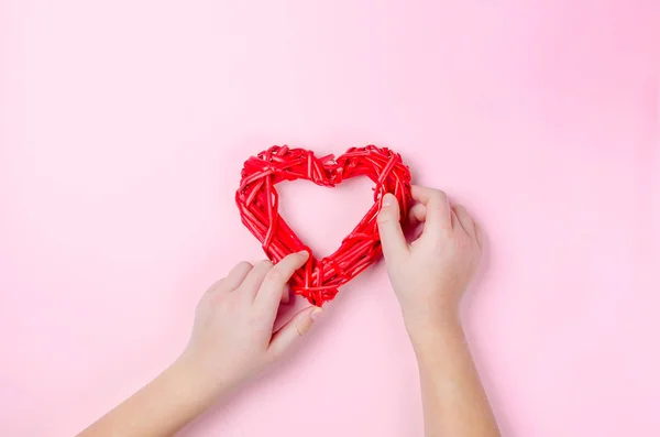 Плетеное сердце из веток в руках девушки на розовом — стоковое фото