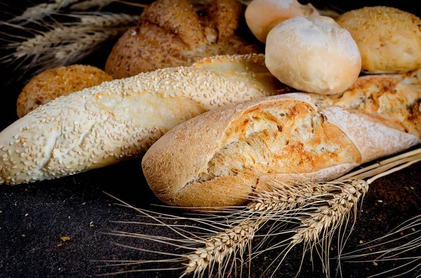Assortment of fresh baked bread with wheat heads on dark wooden table, low key photo, concept healthy or homemade food, for Bakery