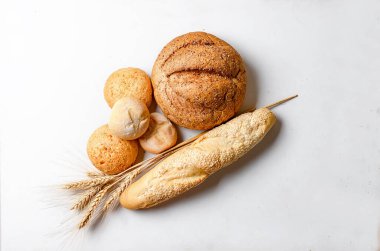 Beyaz masadaki buğday başlıklı taze ekmek çeşitleri, sade fotoğraf, konsept sağlıklı veya ev yapımı yemek, fırın için. 