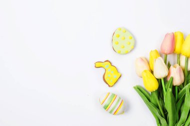 Beyaz arka planda ev yapımı zencefilli kurabiyeler, süslemeli yumurtalar ve laleler. Mutlu Paskalyalar. Boşluğu, düzlüğü, metin için yeri olan şablon düzenleme tebrik kartını kopyala,