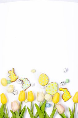 Beyaz arka planda ev yapımı zencefilli kurabiyeler, süslemeli yumurtalar ve laleler. Mutlu Paskalyalar. Boşluğu, düzlüğü, metin için yeri olan şablon düzenleme tebrik kartını kopyala,