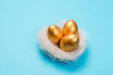 Yuvasında altın süslemeli yumurtalar ve mavi arka planda tüyler olan bir yuva. Bahar tatili konsepti. Boşluğu kopyala, şablon modelleme Paskalya tebrik kartı ile metin için yer, 