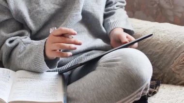 Kulaklık, ders kitabı ve tabletli genç kız evdeki koltukta oturuyor, konsept çevrimiçi öğrenim, eğitim, teknoloji ve internet, gizlilik, mesafe, evde kalmak, salgın sırasında karantina