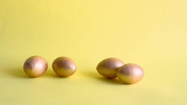 Altın dekoratif yumurtalar yuvarlanıyor ve birbirlerine sarı bir zemin vuruyorlar. Bahar tatili konsepti. Boşluğu kopyala, şablon modelleme Paskalya tebrik kartı 
