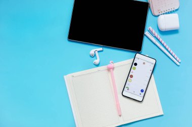 Çevrimiçi eğitim kavramı. Tablet, telefon, kulaklık, defter, mavi arka planda okul malzemeleri. Karantinadaki uzak okul. Kopyalama alanı ile yukarıdan görüntüle. Model, düz yatak..