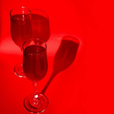 Kırmızı arka planda kırmızı köpüklü kırmızı şarap ve gölgeli iki bardak kokteyl. Minimalist yaratıcı sanat kompozisyonu. Kavramsal görüntü. Basit görsel kavram.