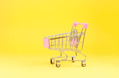 Küçük süpermarketler, sarı renkli arka planda tekerlekleri olan alışveriş için oyuncak arabası satıyorlar. Alışveriş düşkünü, satıcı ya da alıcı, tüketici konsepti.