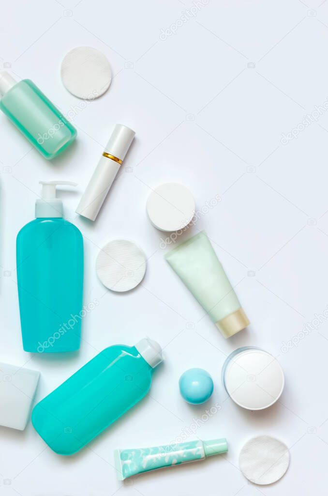 Daily care cosmetics on white background. Flat lay composition with blue and white dispenser, bottles and jars. Beauty products for facial skin care, face cream and lip balm, organic cosmetic.