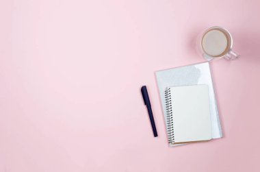 Çalışma masası, boş defterler, malzemeler, bardaklar ve pembe arka planda bir fincan kahve. Metin için boşluk olan üst görünüm. Düz yatıyordu. Asgari tarz ev ofisi ya da Modern Serbest İşyeri.