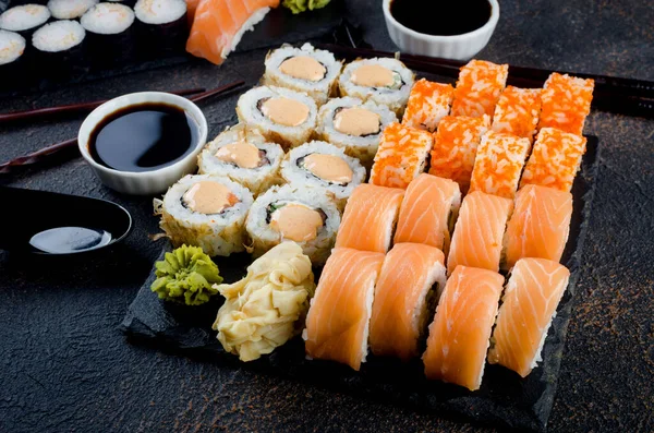 Rolos de sushi saborosos com molhos, gengibre e wasabi no escuro — Fotografia de Stock