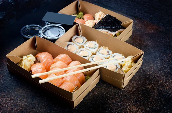 Smakliga sushirullar i engångslådor av kraftpapper, såser, ätpinnar. Sushi för hämtning eller leverans — Stockfoto