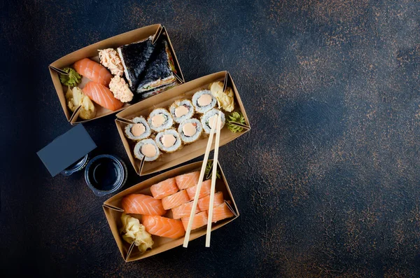 Smakliga sushirullar i engångslådor av kraftpapper, såser, ätpinnar. Sushi för hämtning eller leverans — Stockfoto