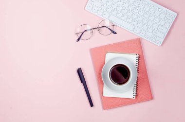 Çalışma masası, boş defterler, malzemeler, bardaklar ve pembe arka planda bir fincan kahve. Metin için boşluk olan üst görünüm. Düz yatıyordu. Asgari tarz ev ofisi ya da Modern Serbest İşyeri.