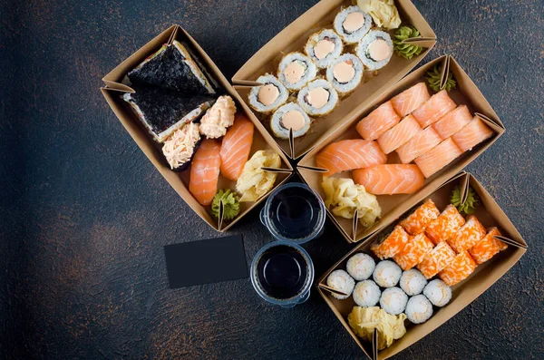 Tasty sushi rolls in disposable kraft paper boxes, sauces on dark table. Concept delivery service Japan food in eco container. flat lay, Template mockup with place for text, Zero waste packaging