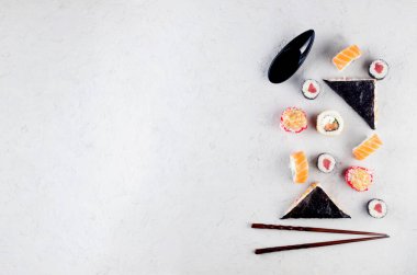 Farklı suşiler ve soya soslu dürümler, zencefil, wasabi ve çubuklar gri beton bir masada. Suşi menüsü. Japon yemeği servisi. Moda melezi gıdaları.