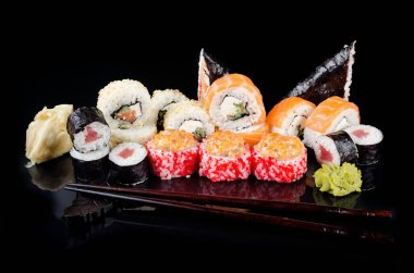 Farklı suşi ruloları, soya sosu, zencefil, wasabi ve çubukları siyah bir masada. Asya restoranı suşi menüsü. Japon yemeği servisi. Düz yatış, metin için yeri olan şablon modeli, 