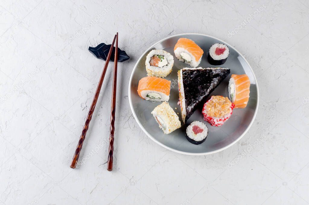Assorted different sushi rolls on a plate and soy sauce, ginger, wasabi and chopsticks on a gray concrete table.Asian restaurant menu. Delivery service Japanese food. Template mockup, place for text