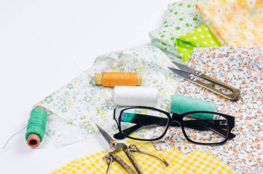 Renkli sarı ve yeşil kumaşlar, makas, düğmeler, iplik makaraları ve beyaz üzerine gözlük. Terzilik, yama ve el işi kavramı. Dikiş ve dikiş..