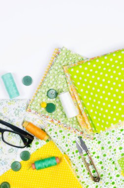 Renkli sarı ve yeşil kumaşlar, makas, düğmeler, iplik makaraları ve beyaz üzerine gözlük. Terzilik, yama ve el işi kavramı. Dikiş ve dikiş..