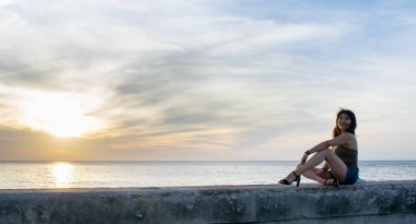 Günbatımına bakan genç bir kadın Küba, Havana 'da iskelede oturuyor.