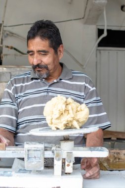 Nixtamal değirmeninde hamur satan bir adam. Hamuru tartmak için sarkaç kullanılıyor..