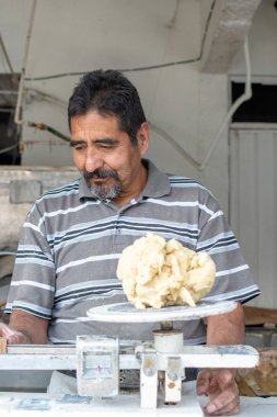 Nixtamal değirmeninde hamur satan bir adam. Hamuru tartmak için sarkaç kullanılıyor..
