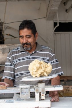Nixtamal değirmeninde hamur satan bir adam. Hamuru tartmak için sarkaç kullanılıyor..