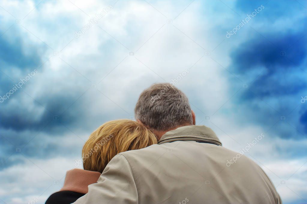 back view to an elderly couple. the woman put her head on the man's shoulder. against a background of a deep blue sky.
