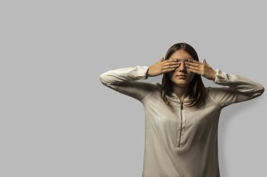 uzun saçlı genç güzel öğrenci kız portresi. gözleri onun ellerde ile kaplı. metin için yer çok. gri bir arka plan üzerinde izole.