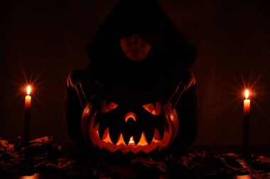 siyah başlıklı bir kadın onun ellerini korkunç parlayan Cadılar Bayramı Balkabağı üzerinde tutar..