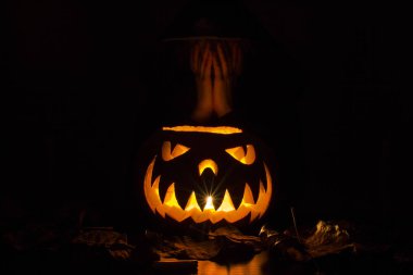 siyah kukuleta gelinin yüzünü elleriyle üzerinde ışık saçan korkunç Cadılar Bayramı Balkabağı kaplı.