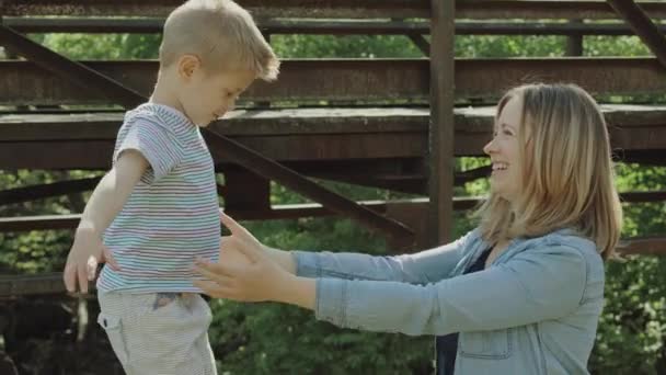 Beautiful young mom and cheerful adorable blond boy are playing, having fun. Woman loves her son. Beautiful young mom and cheerful adorable blond boy are playing in the park — ストック動画