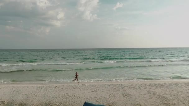 Vista superior de la mujer en bikini corre a lo largo de la playa. Vista aérea de la dama delgada cerca del océano en sus vacaciones — Vídeos de Stock