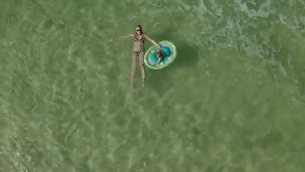 Young woman with a little girl swimming together in the ocean. View from above of the baby girl with swimming circle floating together with mother — 비디오