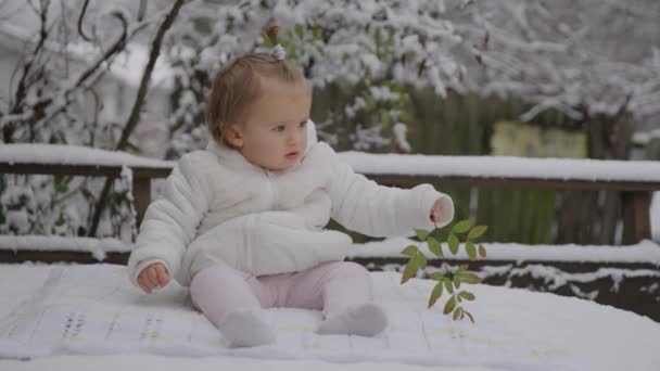 Gelukkig lachend meisje zittend in het snowpark. Klein kind geniet van de allereerste sneeuw. — Stockvideo