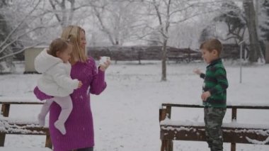 Çocuklarıyla birlikte kar parkında eğlenen genç sarışın kadın.