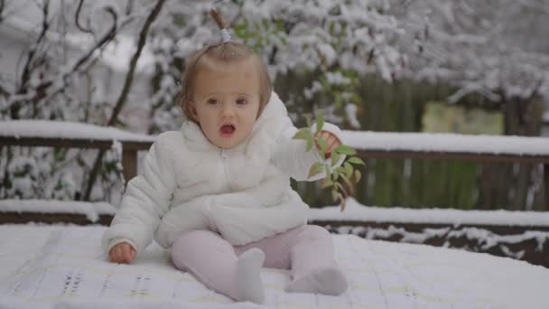 Feliz menina sorridente sentada no parque de neve. Criança desfrutando da primeira neve . — Vídeo de Stock