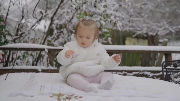 Feliz menina sorridente sentada no parque de neve. Criança desfrutando da primeira neve . — Vídeo de Stock